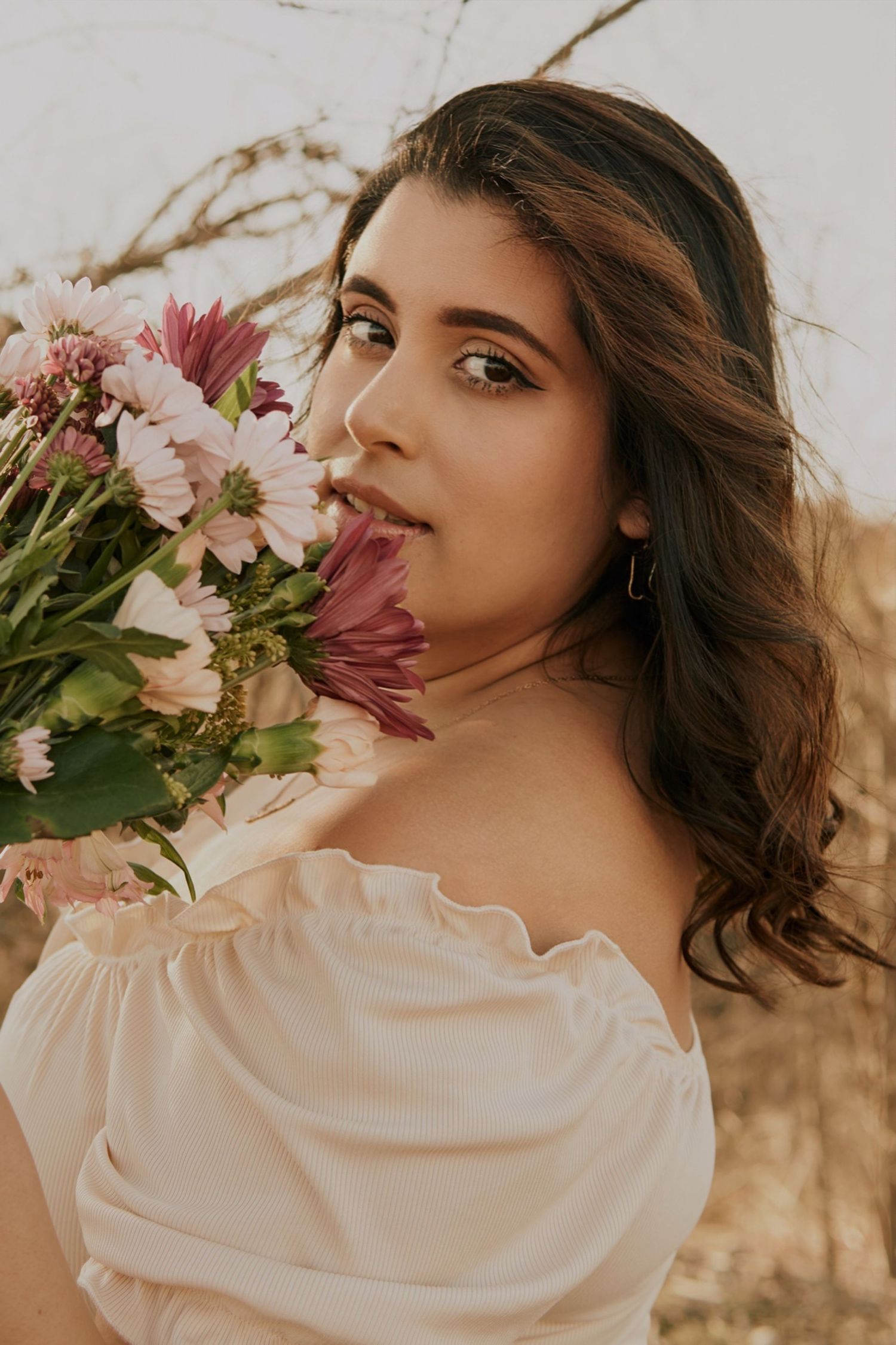Soft portrait with pink and white flowers against a natural background in warm golden light and cream dress.
