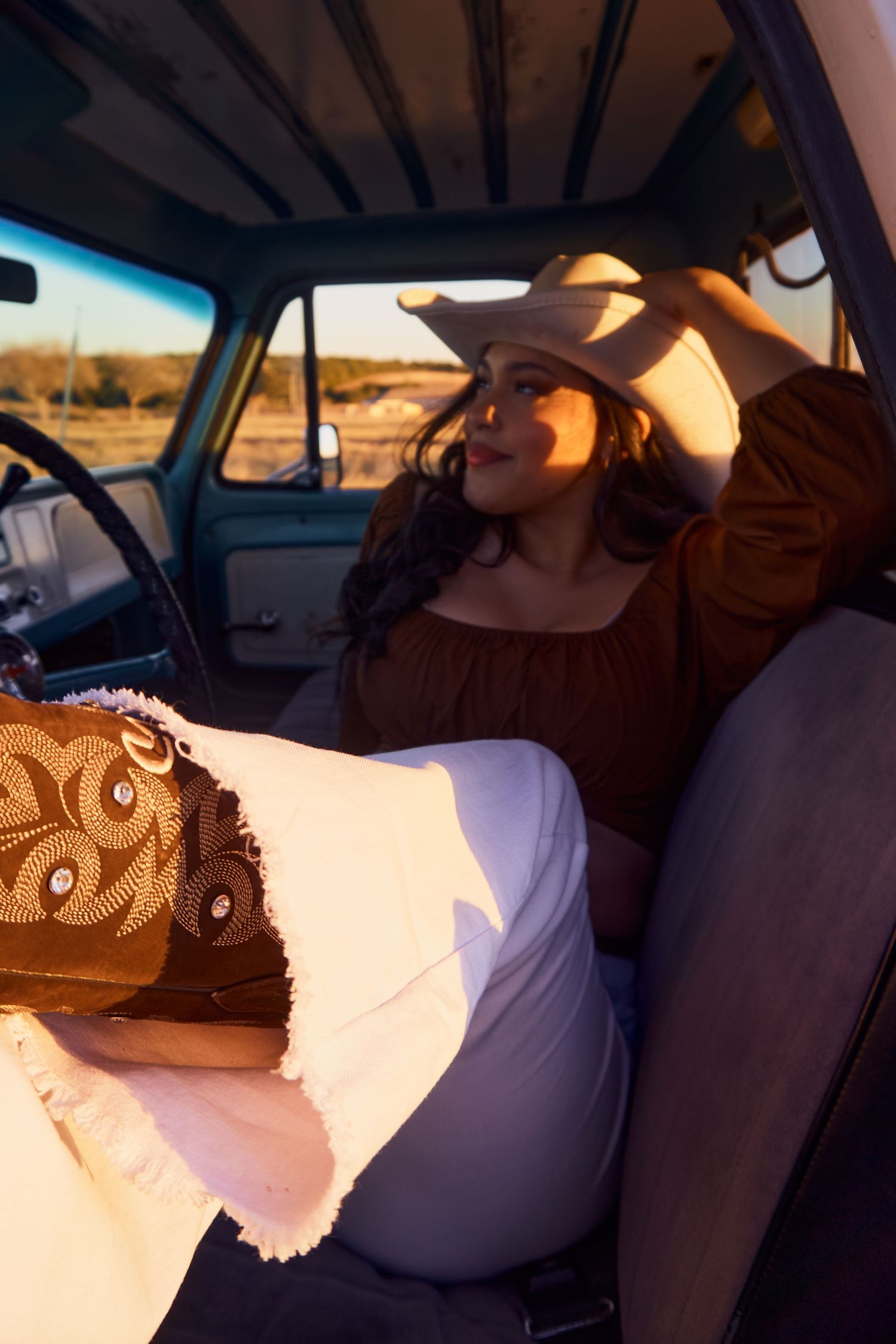 Vintage-style photo inside truck cab wearing western hat during golden hour.