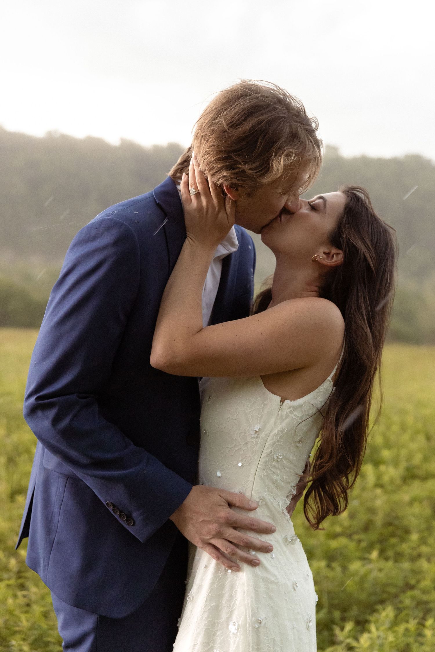 Couple shares romantic kiss in the rain during outdoor wedding ceremony in green field.