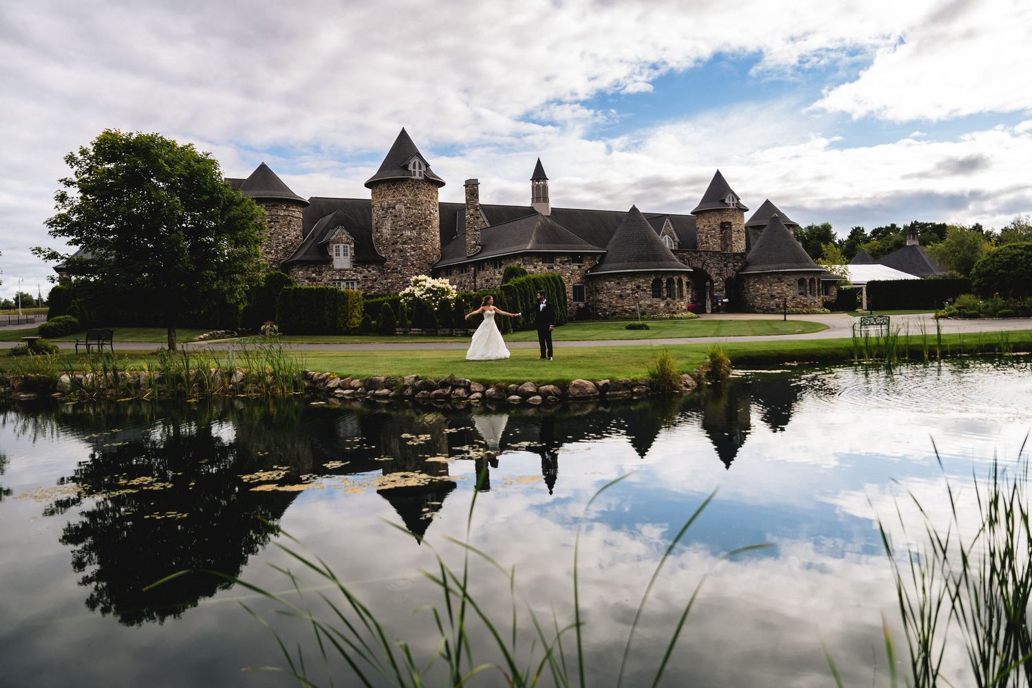 Stone castle venue with reflecting pond creates a romantic wedding day setting under blue skies.