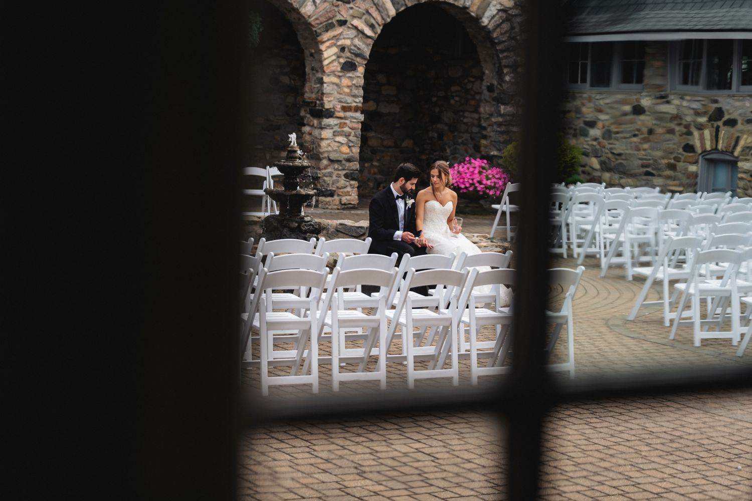 Bride and groom share a quiet moment among white chairs at an outdoor stone venue wedding ceremony.