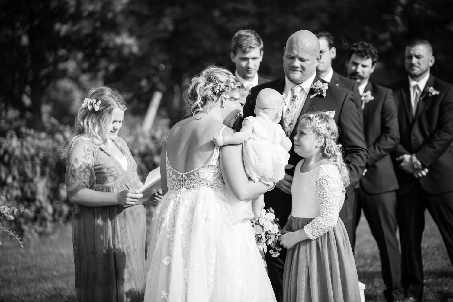 A joyful wedding party laughs together during outdoor photos in a garden setting.