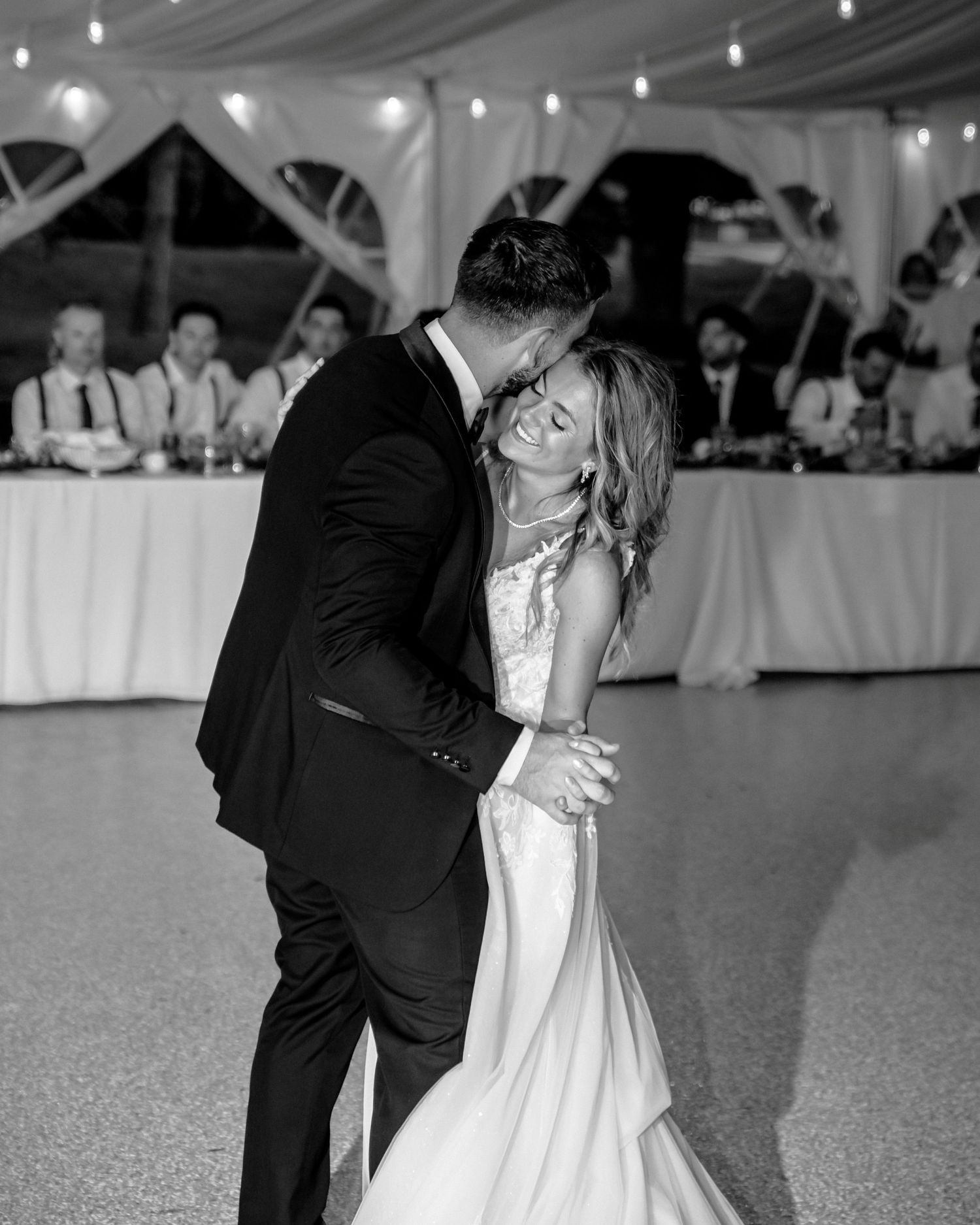 Black and white photo of a bride and groom sharing their first dance at a wedding reception.