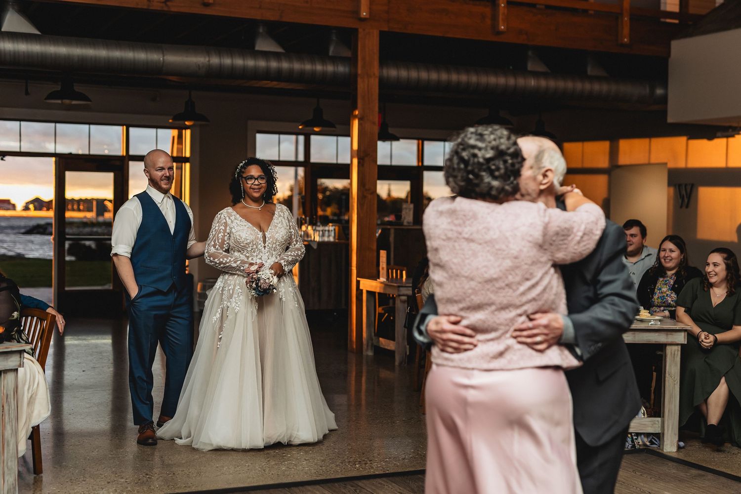 Bride and groom watch as elderly guests share a sweet dance at their rustic wedding reception venue.