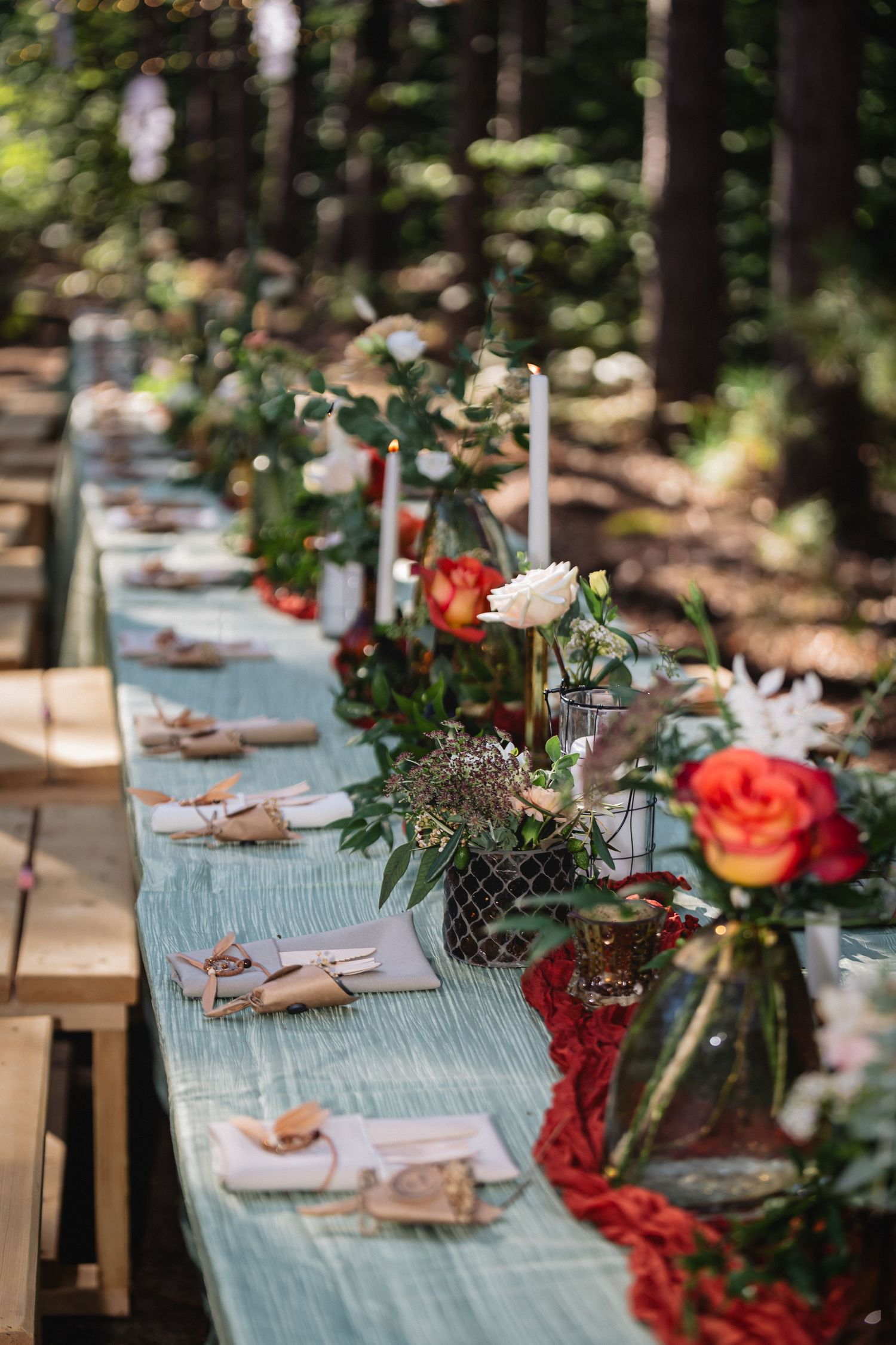 Rustic outdoor table setting with turquoise runners, floral centerpieces and coral roses in a woodland setting.