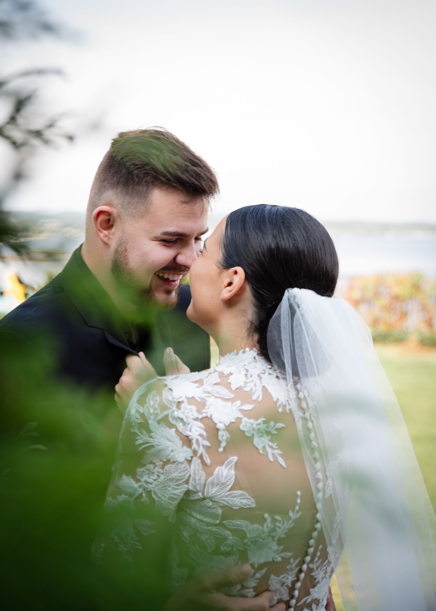 A romantic wedding couple shares an intimate moment in a field with soft natural lighting and delicate lace details.