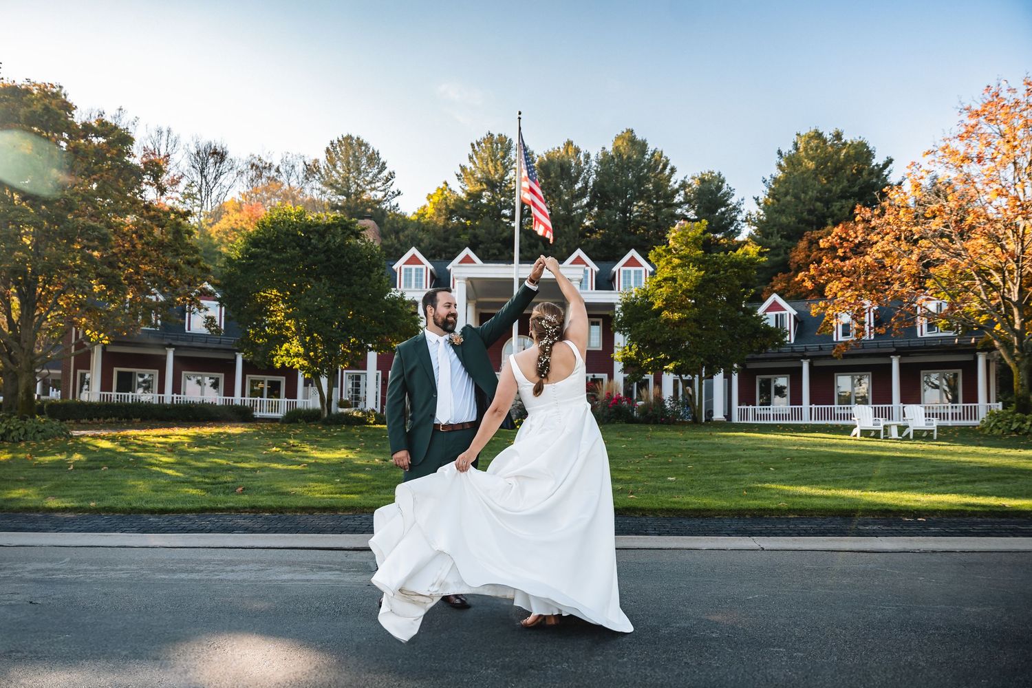 Bride and groom dancing outdoors in front of a grand New England estate with fall foliage and American flag.