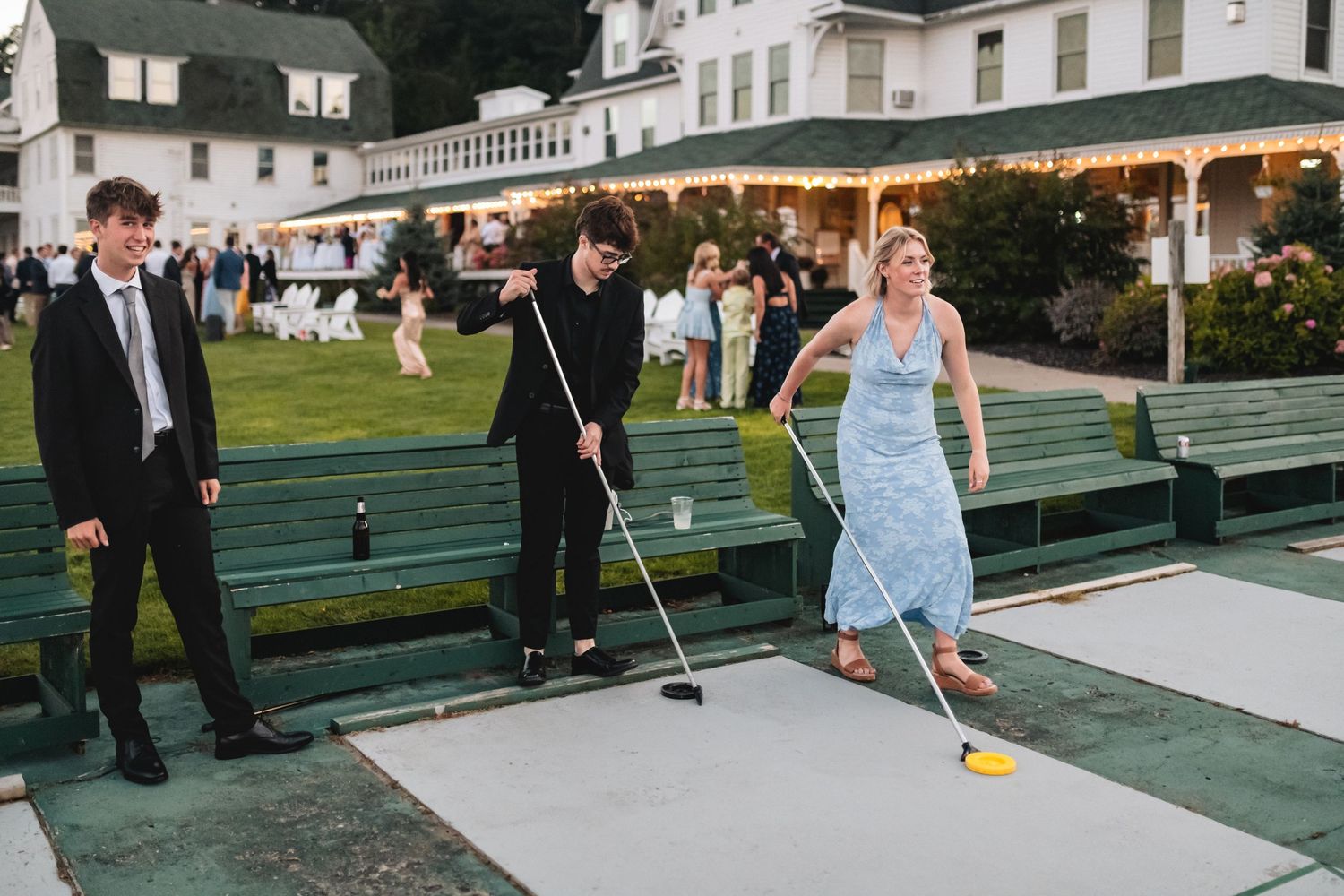 People play miniature golf on a putting green at an outdoor wedding reception with string lights overhead.