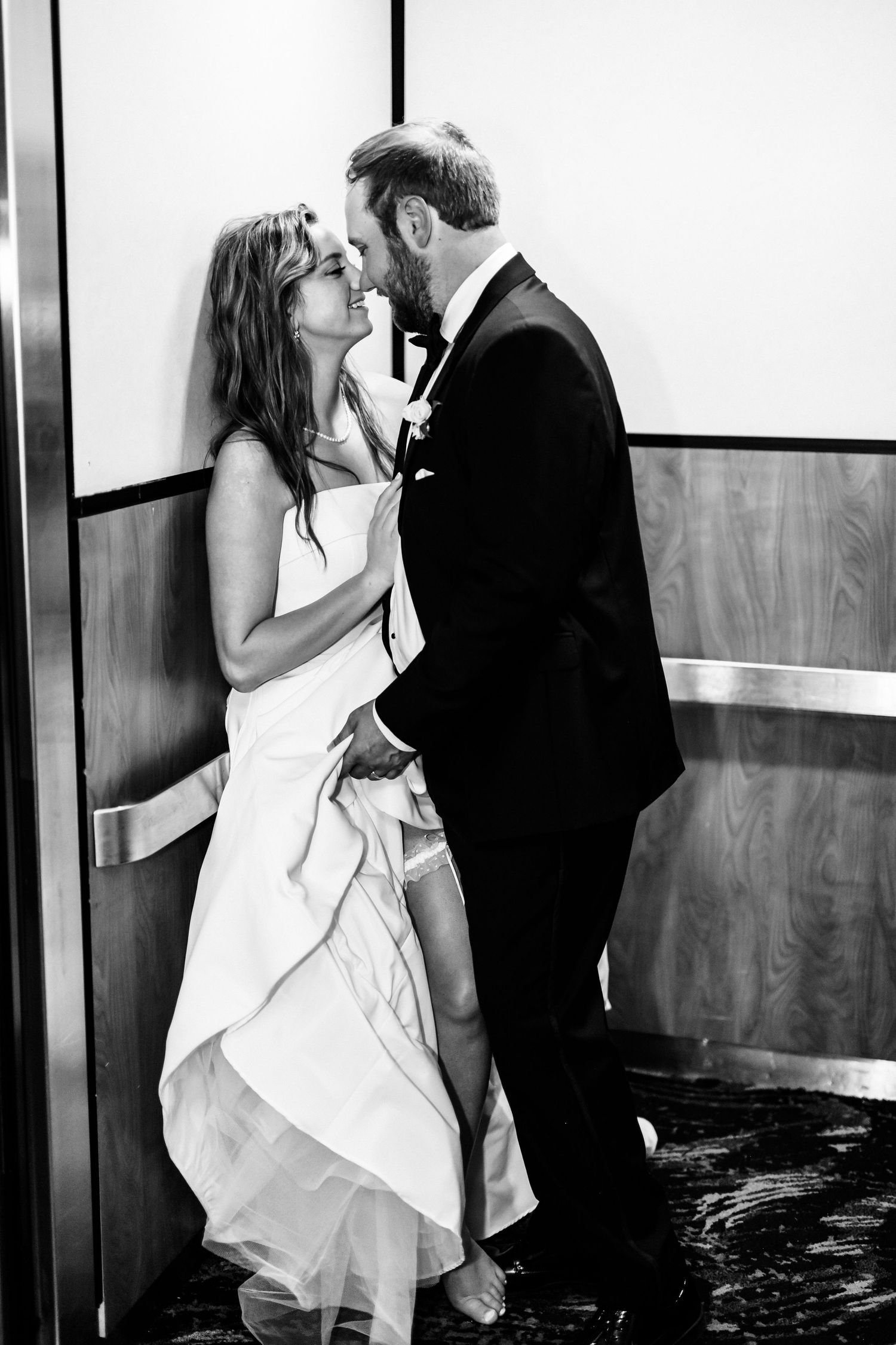 A romantic black and white wedding photo of a couple sharing an intimate moment against a wall.