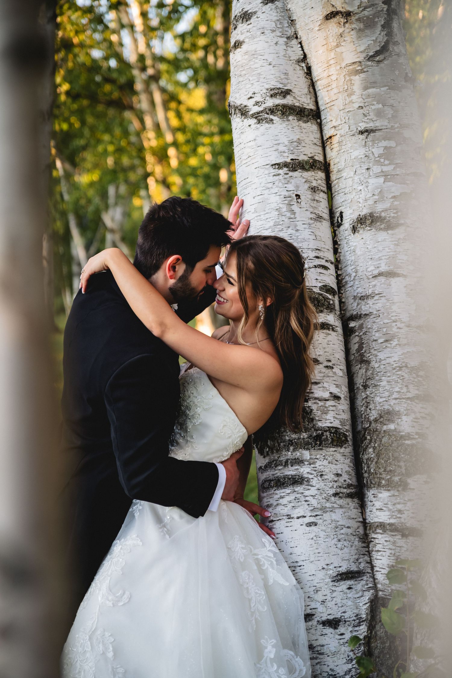 Bride and groom sharing a romantic moment leaning against birch trees in a forest wedding photo.