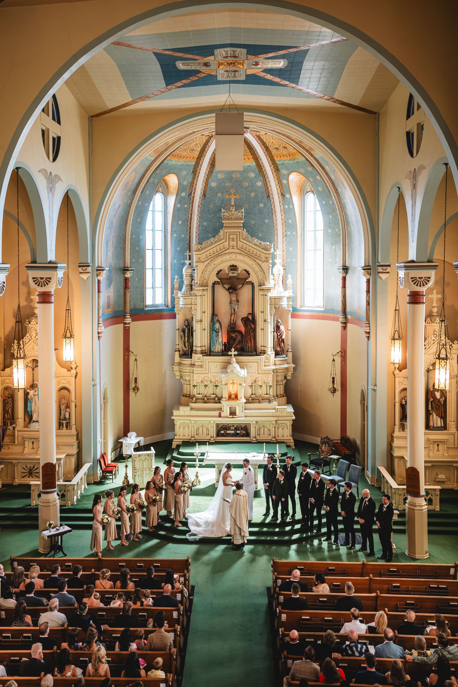 Interior view of a traditional Catholic church with green carpeting, wooden pews, and ornate altar during a ceremony.