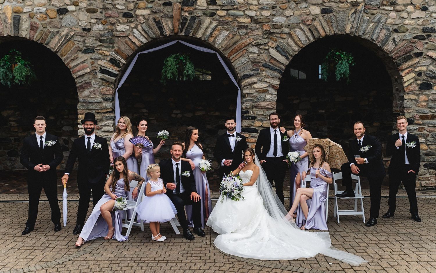 A wedding party poses in front of a stone archway during an outdoor celebration.