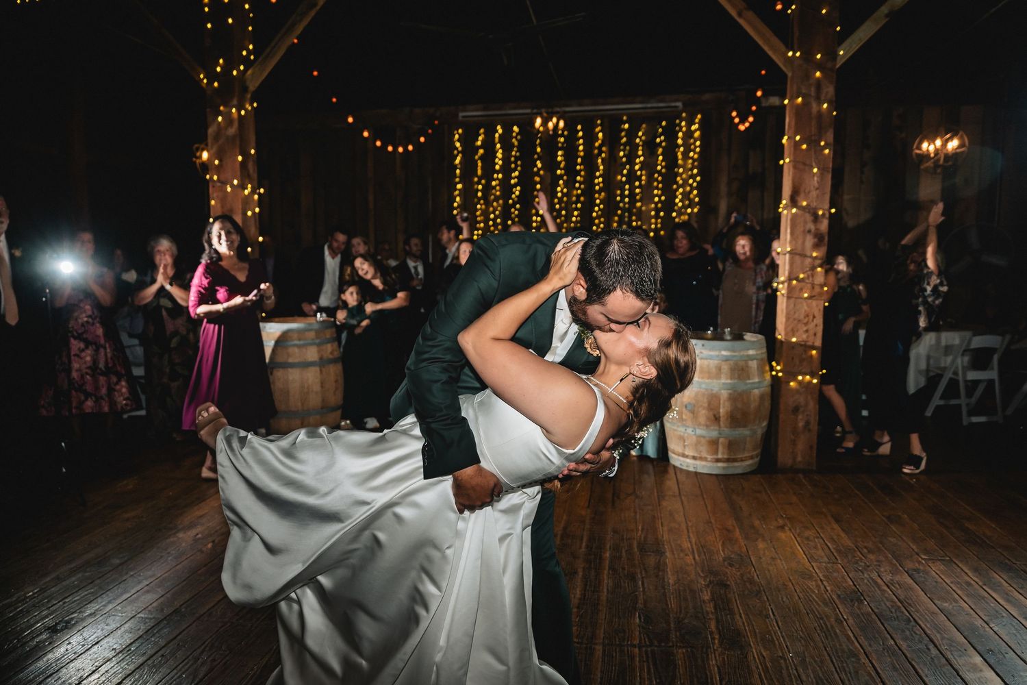 Romantic couple dancing at an elegant wedding reception with string lights and rustic decor in the background.
