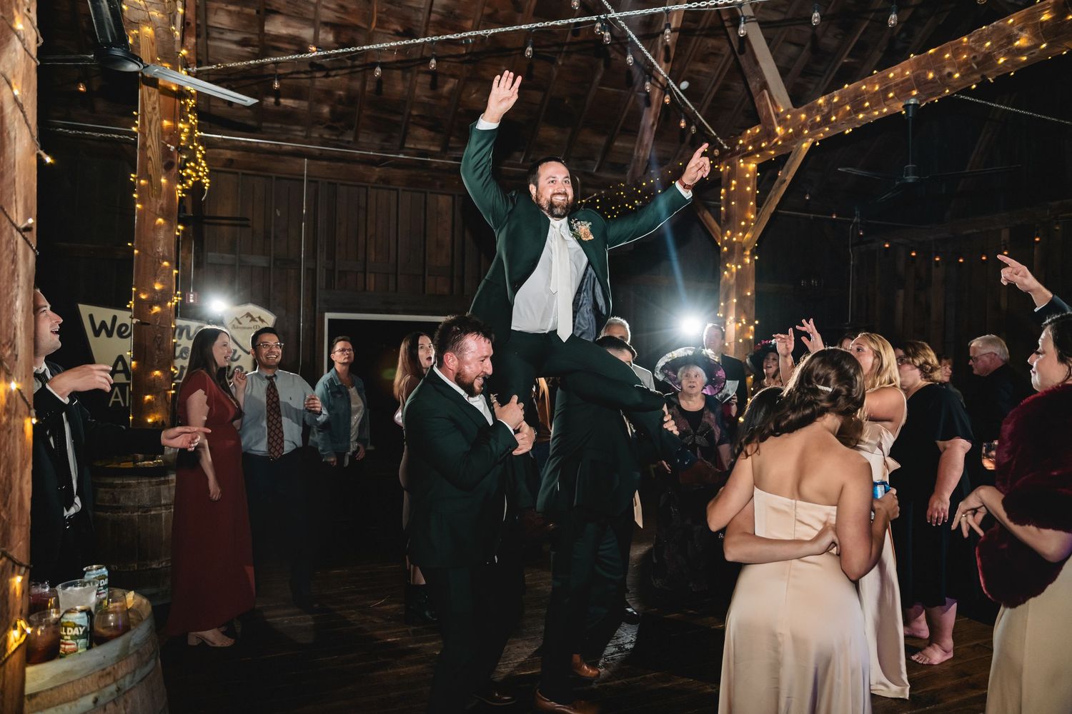Wedding guests dance and celebrate on a dimly lit dance floor decorated with string lights during an evening reception.