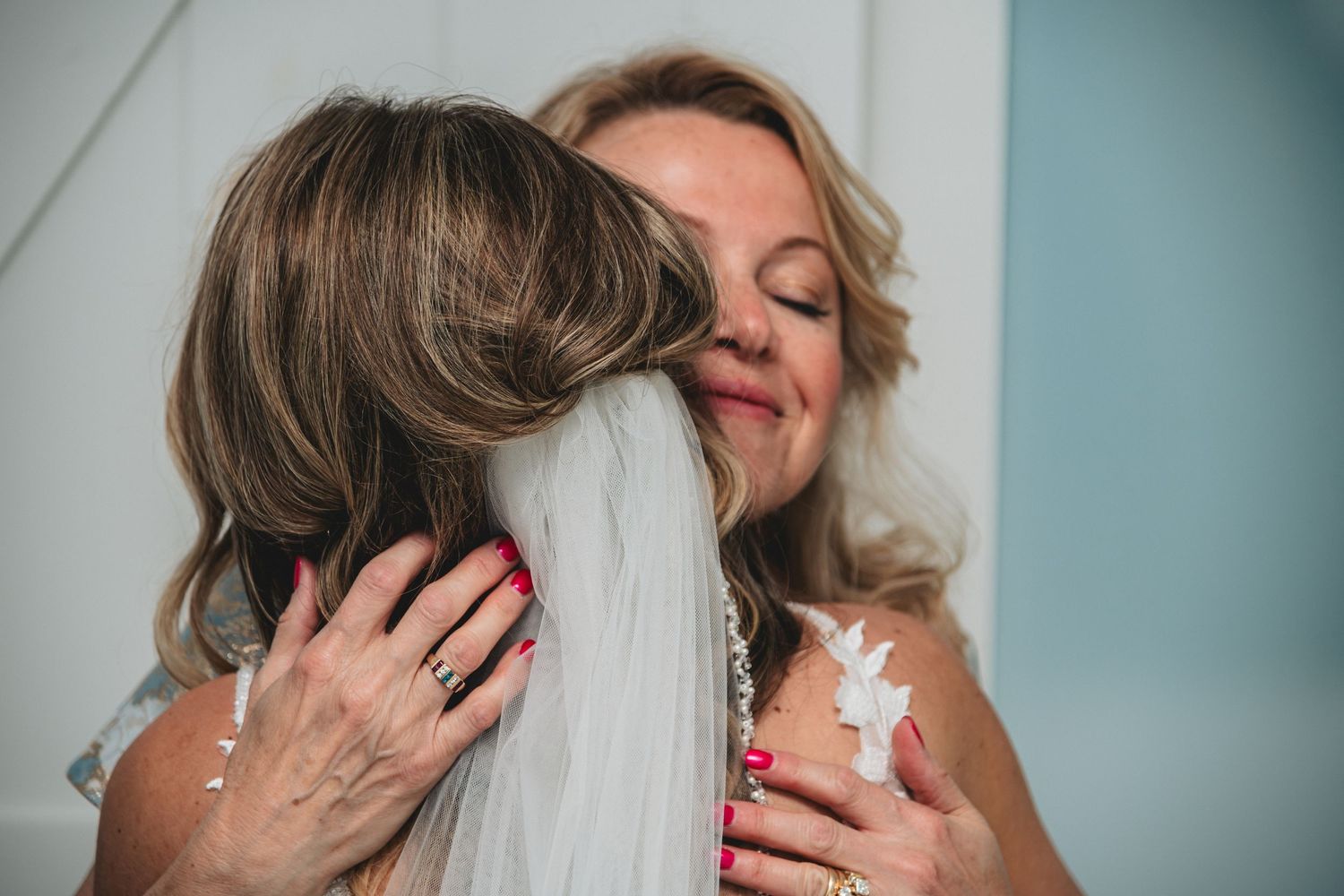A bride in a veil shares an emotional hug with an older woman in a heartfelt wedding moment.