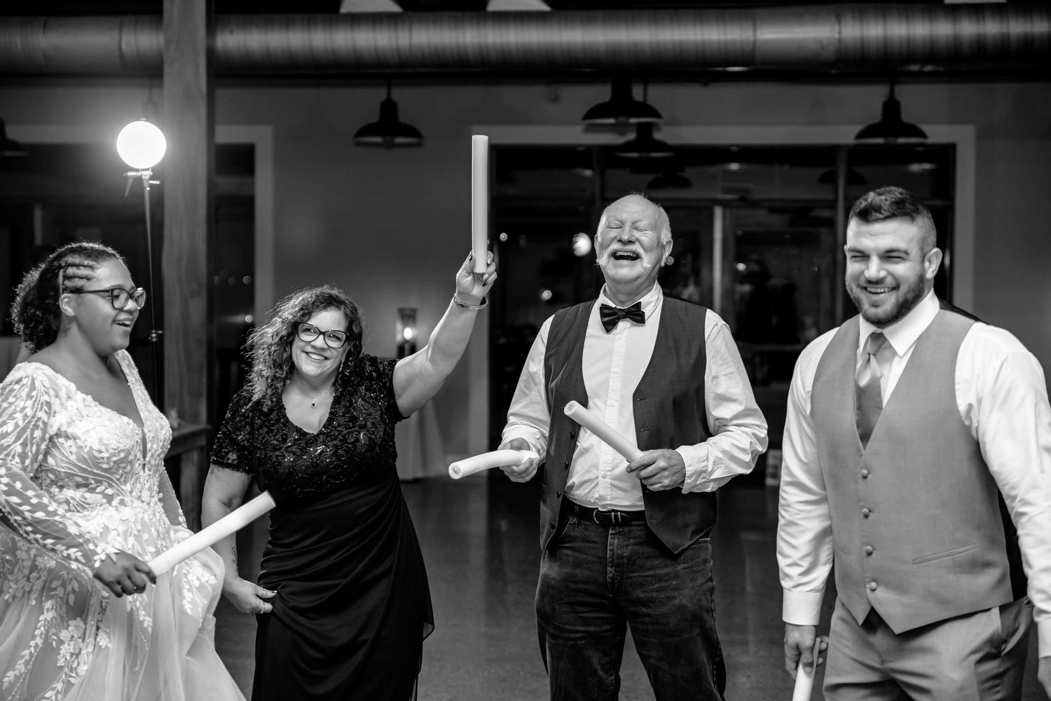 A joyful group dances and celebrates together at a wedding reception in black and white.