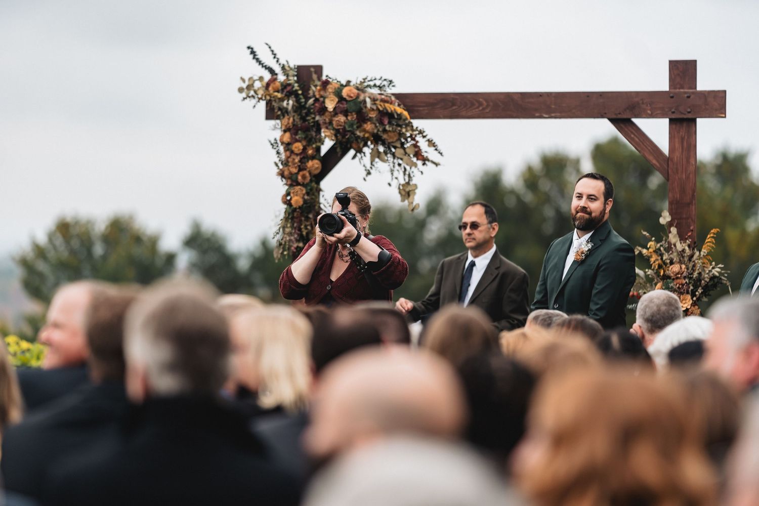 A large wooden cross is held up during an outdoor religious ceremony with a crowd gathered around it.