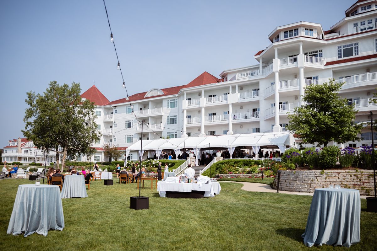 Elegant outdoor wedding reception setup with white linens and coastal resort buildings in the background.