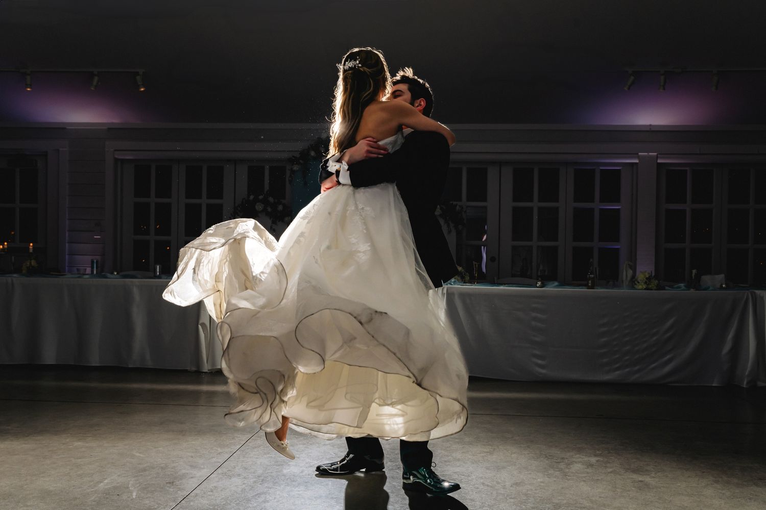Groom lifting bride in white gown during romantic first dance at elegant wedding reception venue.
