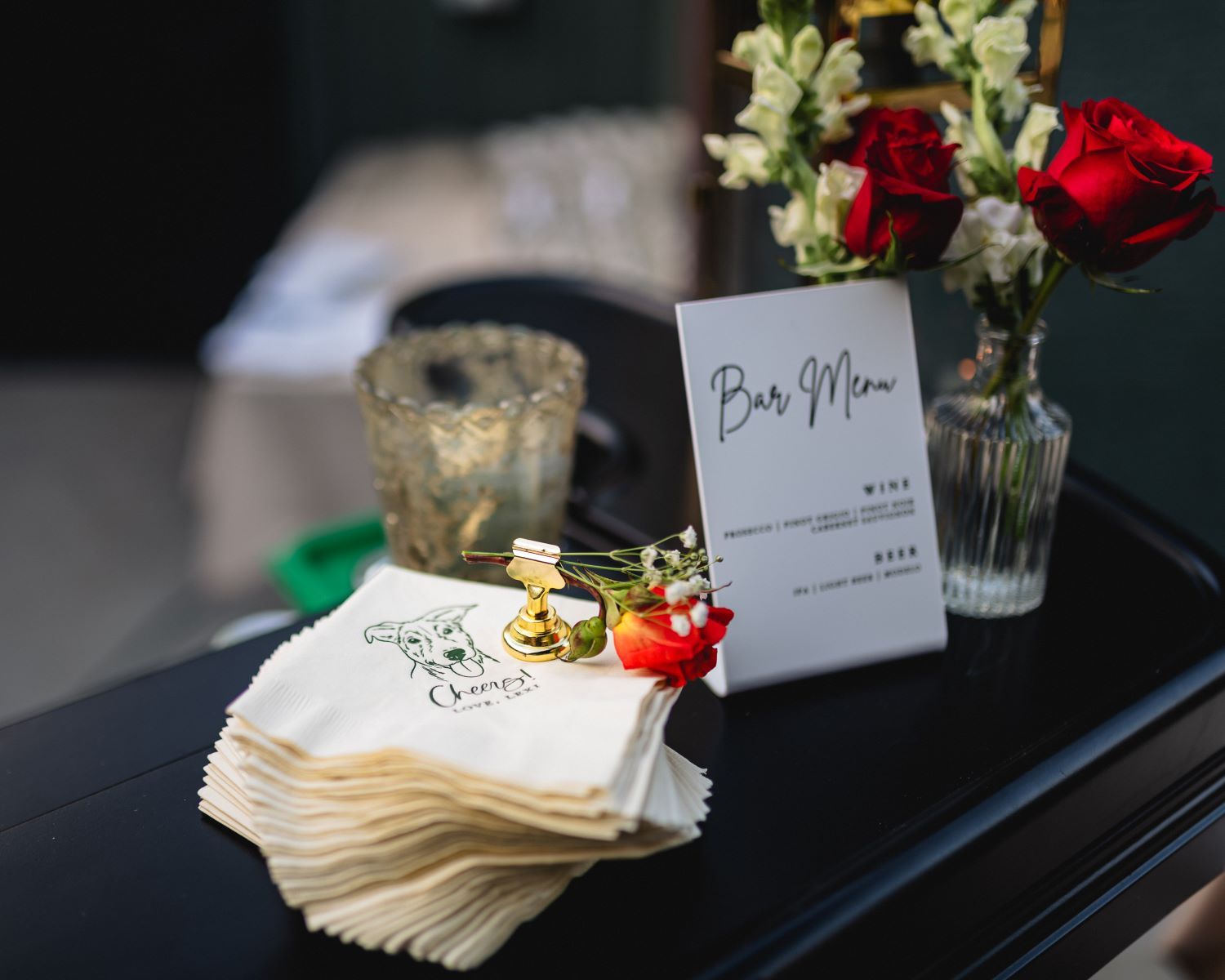 Elegant wedding place cards and floral centerpieces with red and white flowers arranged on a dark table.