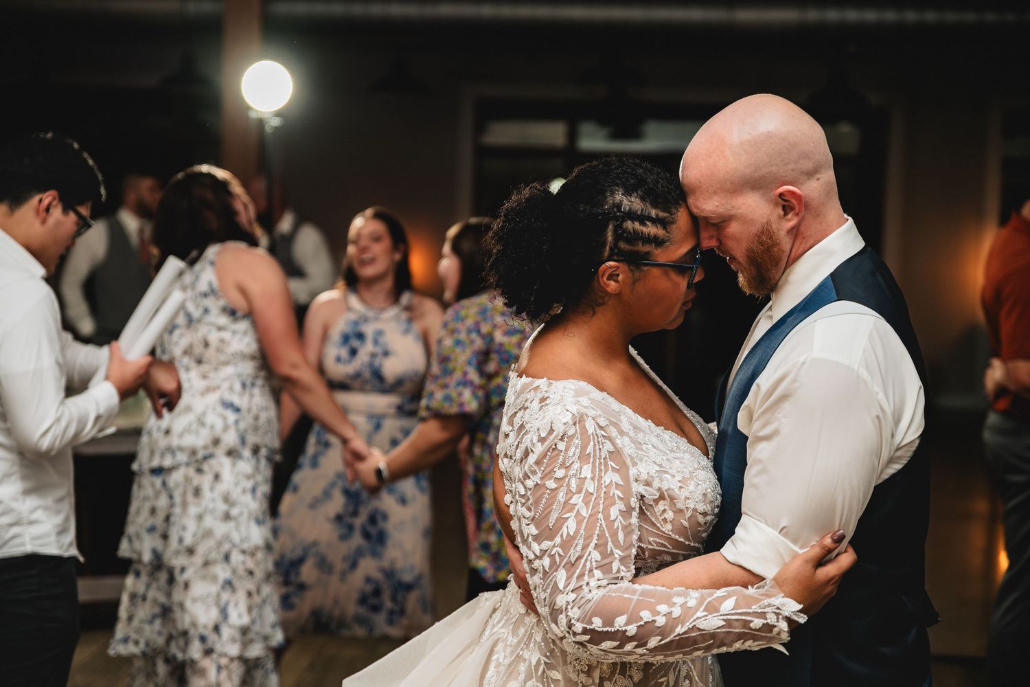 Wedding guests dance and celebrate together on a dimly lit dance floor at an evening reception.