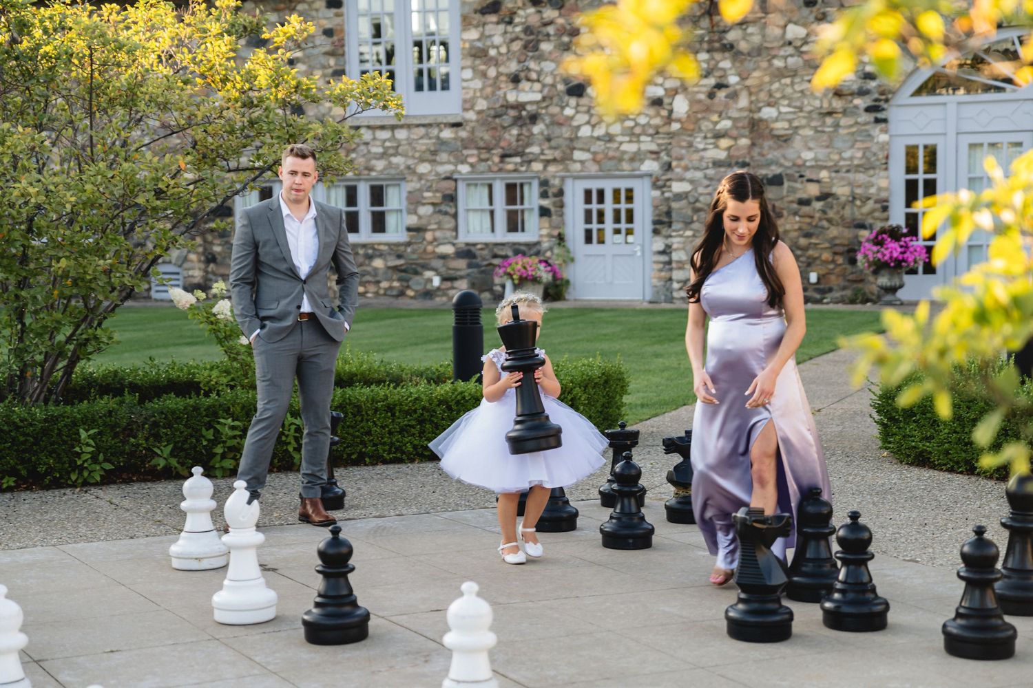 Large outdoor chess pieces decorate a stone patio area with yellow flowers in the foreground.