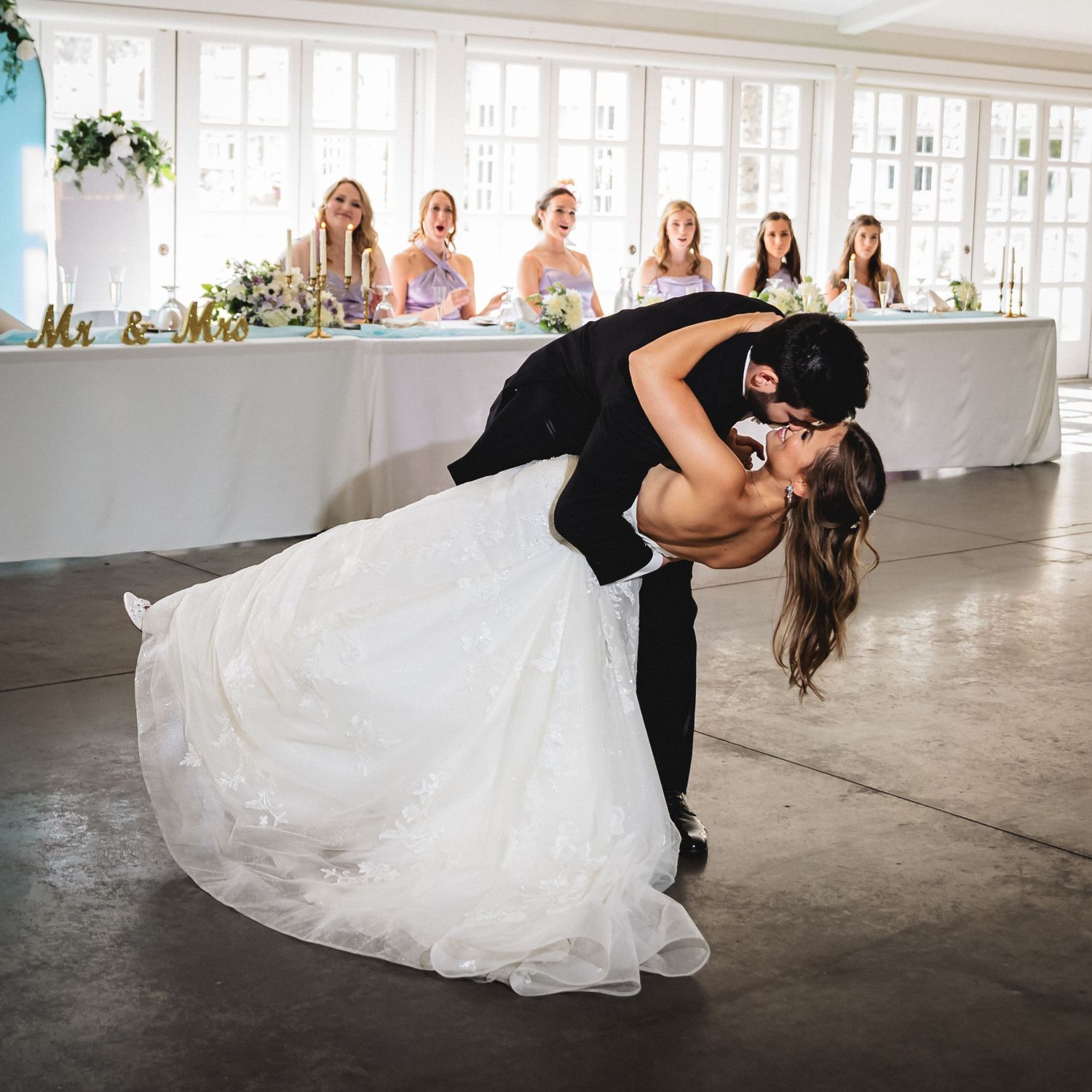 Romantic dip pose sequence of couple in wedding attire dancing in bright industrial space with large windows.
