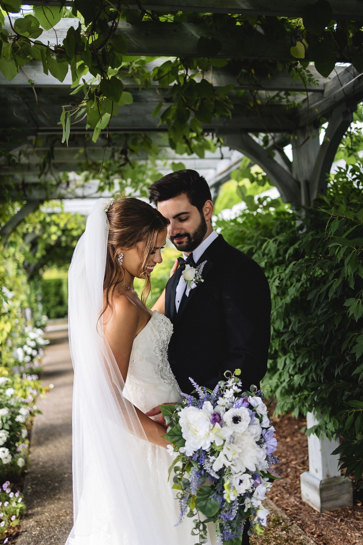 Romantic garden wedding portraits with white and purple floral arrangements under lush green vines.