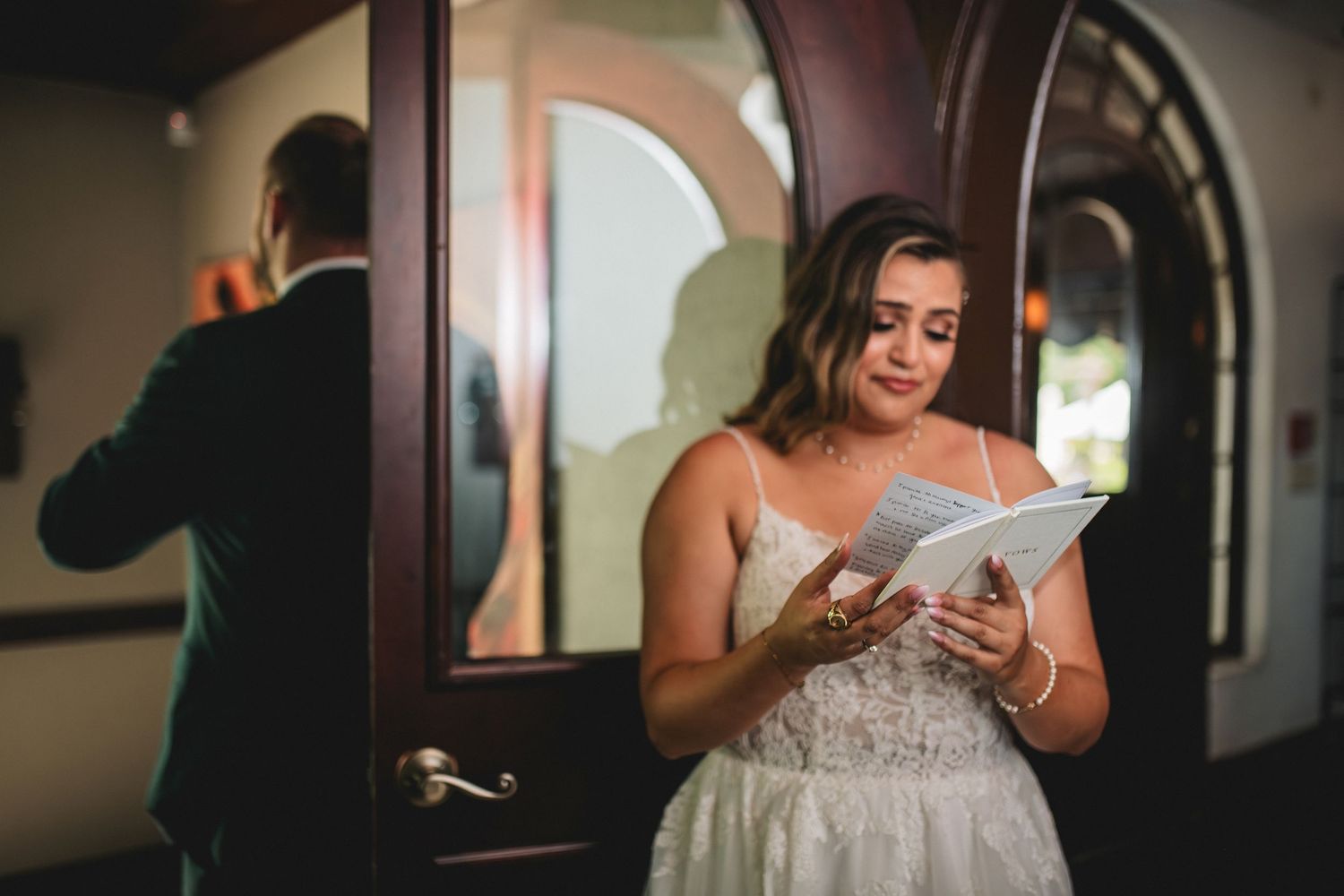 A bride in a white wedding dress adjusts her veil while looking in a mirror during wedding preparations.