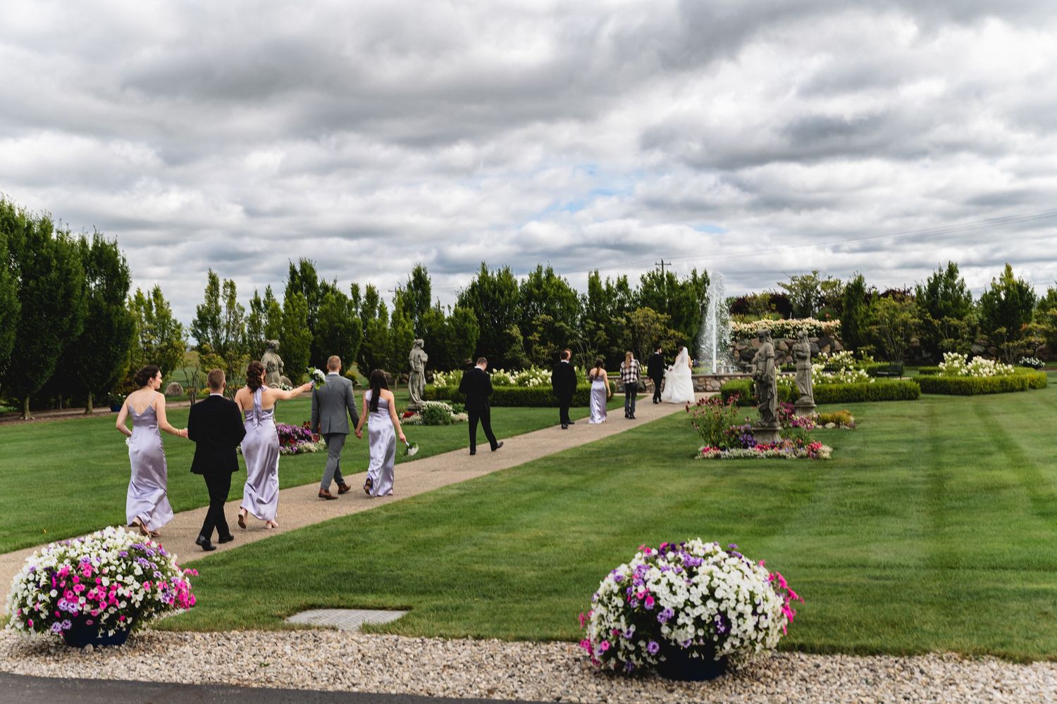 Outdoor wedding venue with pink floral arrangements lining a stone walkway under cloudy skies.
