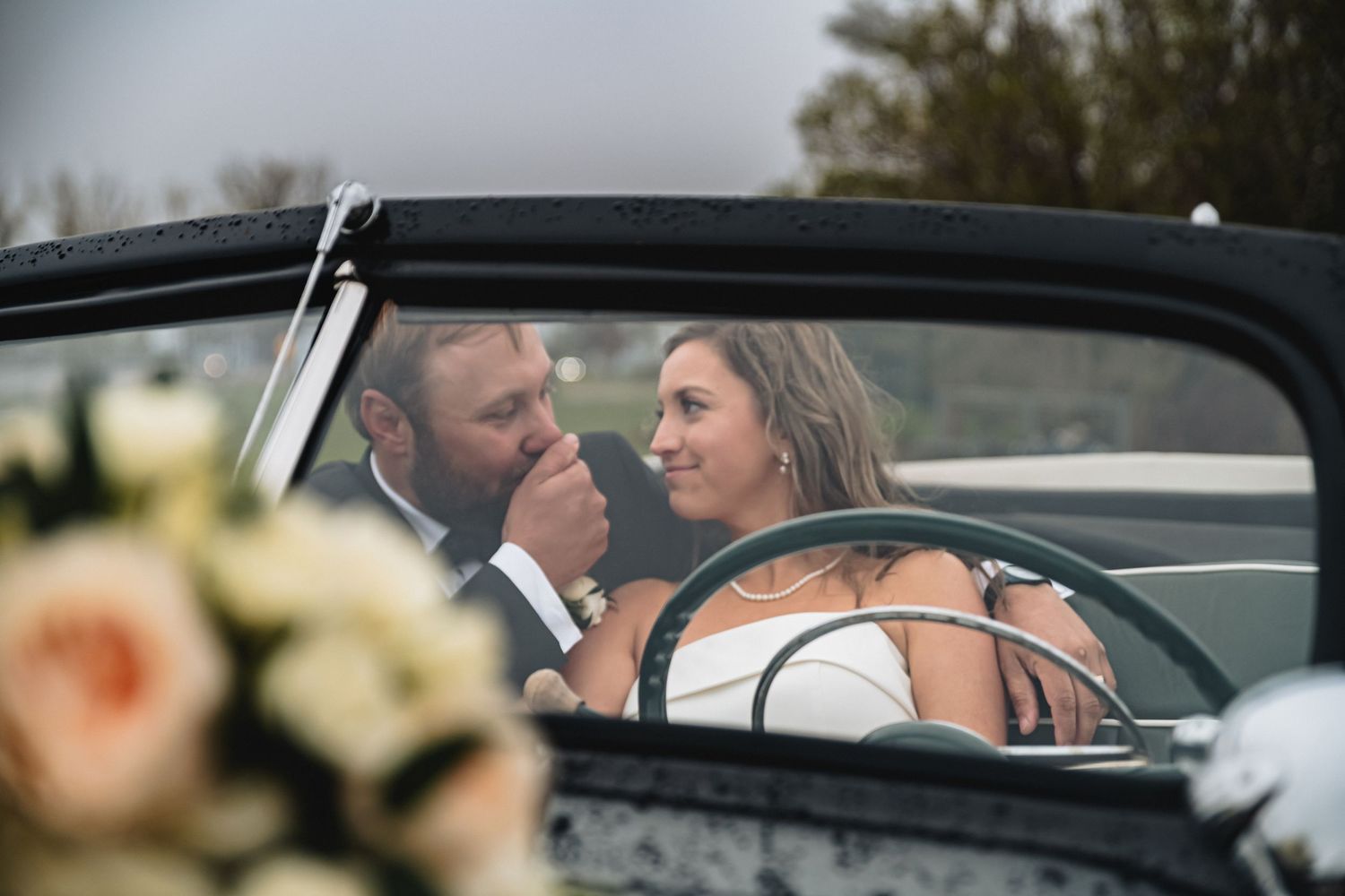 Bride and groom share a romantic moment in a vintage convertible car on their wedding day.