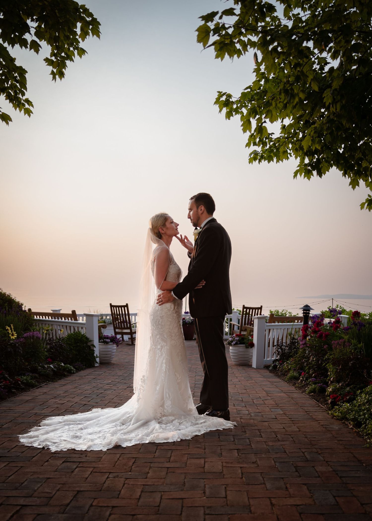 Bride and groom share a romantic moment at sunset on a brick path surrounded by lush gardens and ocean views.