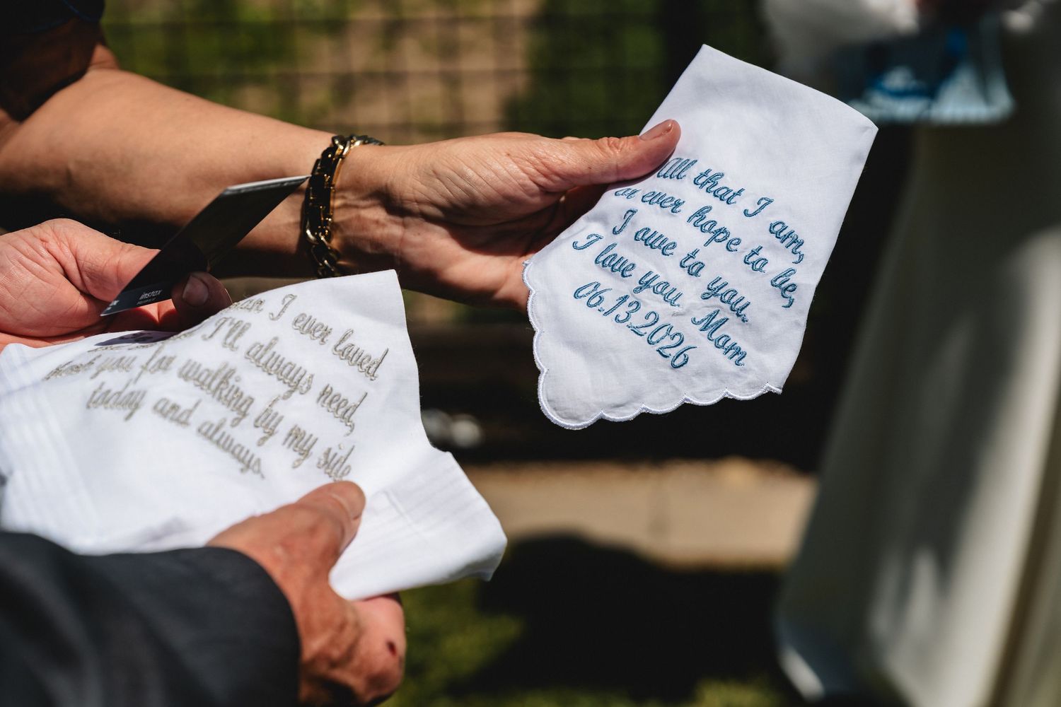 Close-up of hands holding embroidered wedding handkerchiefs with heartfelt messages, a sentimental bridal gift tradition.