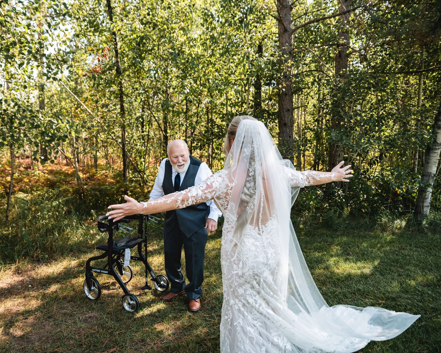 A northern Michigan Bride in a lace wedding gown with long veil opens her arms toward her grandpa for a hug.