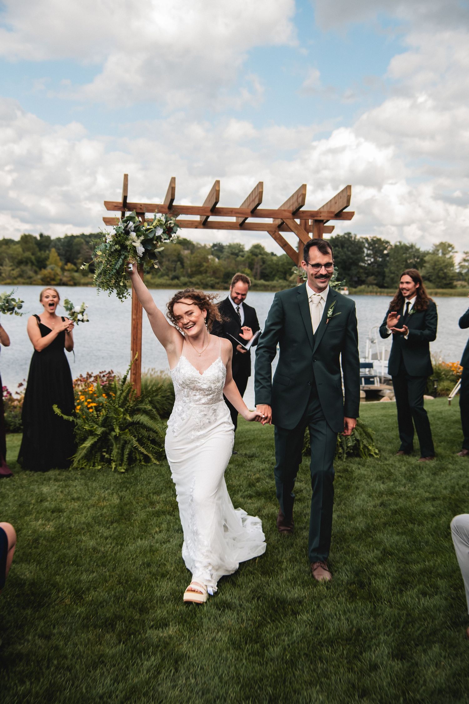 Joyful bride and groom walk down outdoor aisle after wedding ceremony by a lake, surrounded by guests at their up north backyard wedding