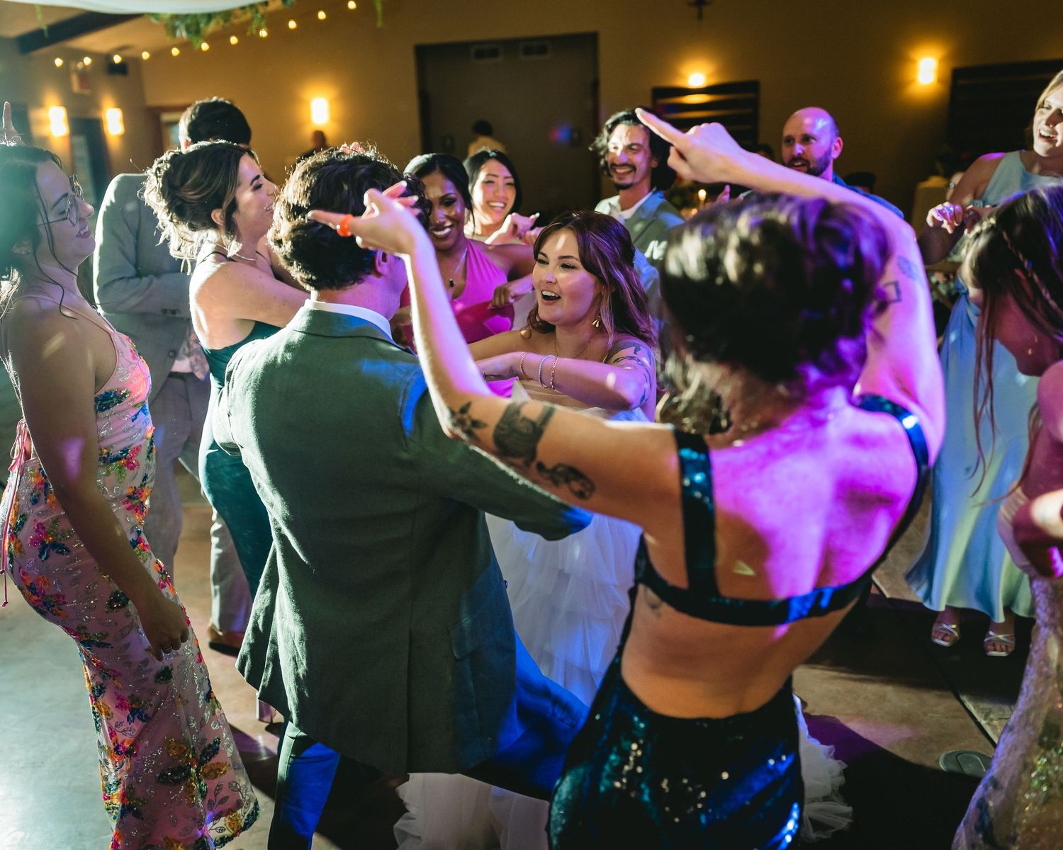Guests dancing joyfully at a lively wedding reception with colorful lighting and festive atmosphere.