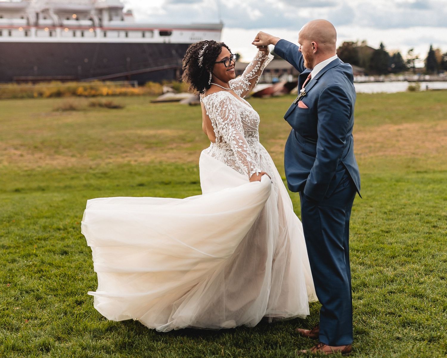 A romantic wedding couple dances together in an open field with flowing white dress and navy suit.