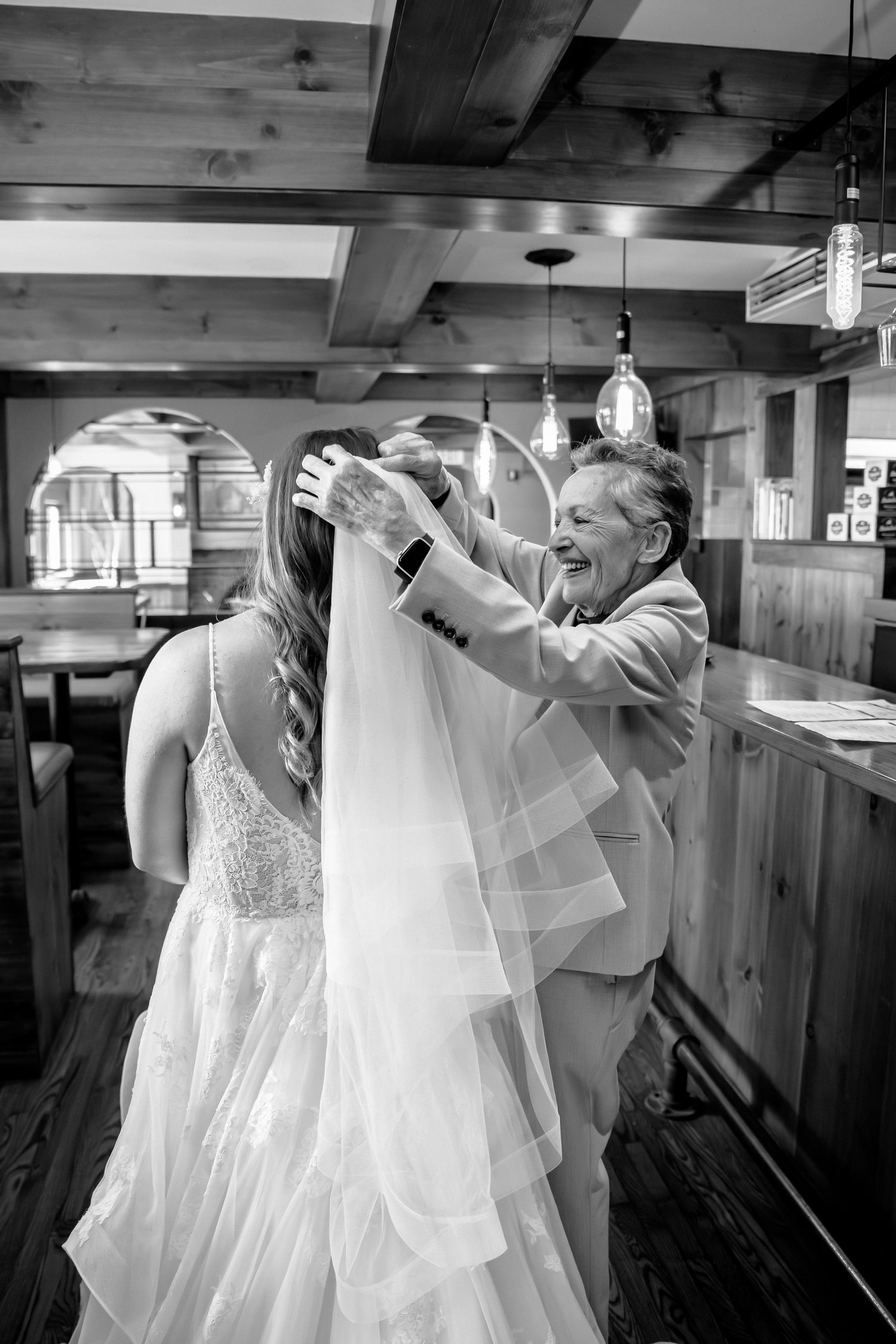 Black and white photo of grandma helping a bride put on her veil inside a northern Michigan venue.