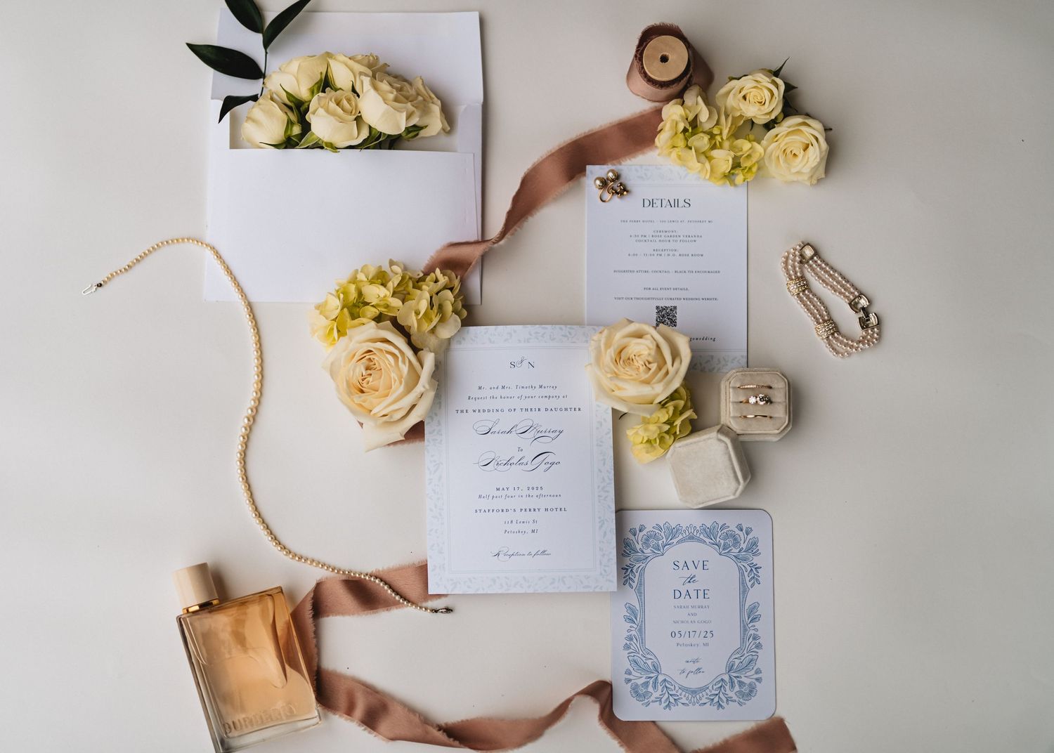 Elegant wedding invitation suite with white and yellow roses, silk ribbons, and blue floral stationery on a white background.