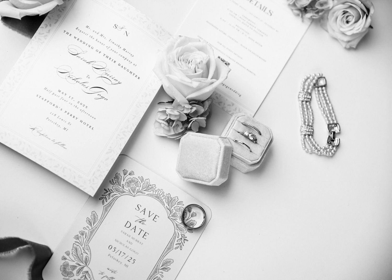 Elegant wedding invitation suite with white roses and delicate stationery laid out on light surface in monochromatic style.