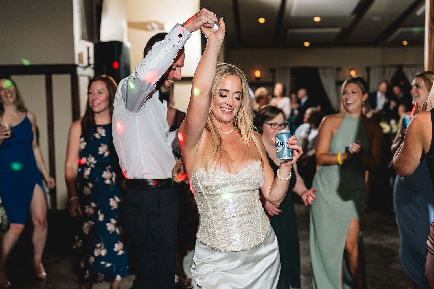 Bride and groom dancing joyfully at wedding reception surrounded by guests celebrating on the dance floor.