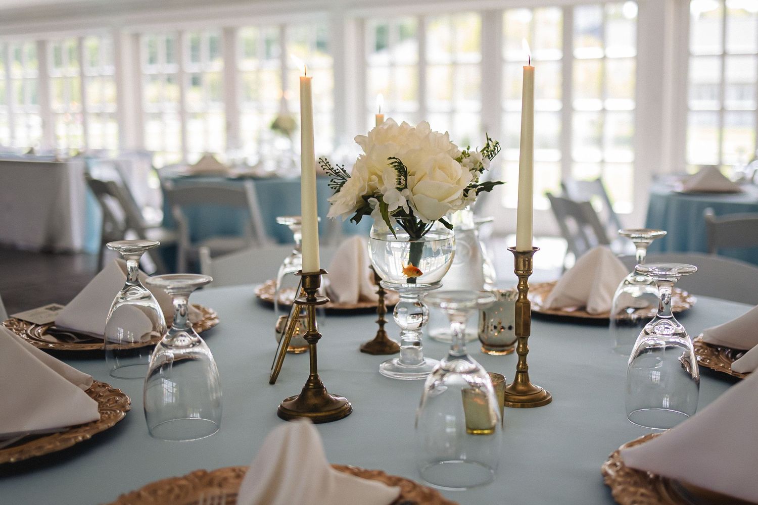 Elegant table settings with gold candelabras and white linens in a light-filled reception room.