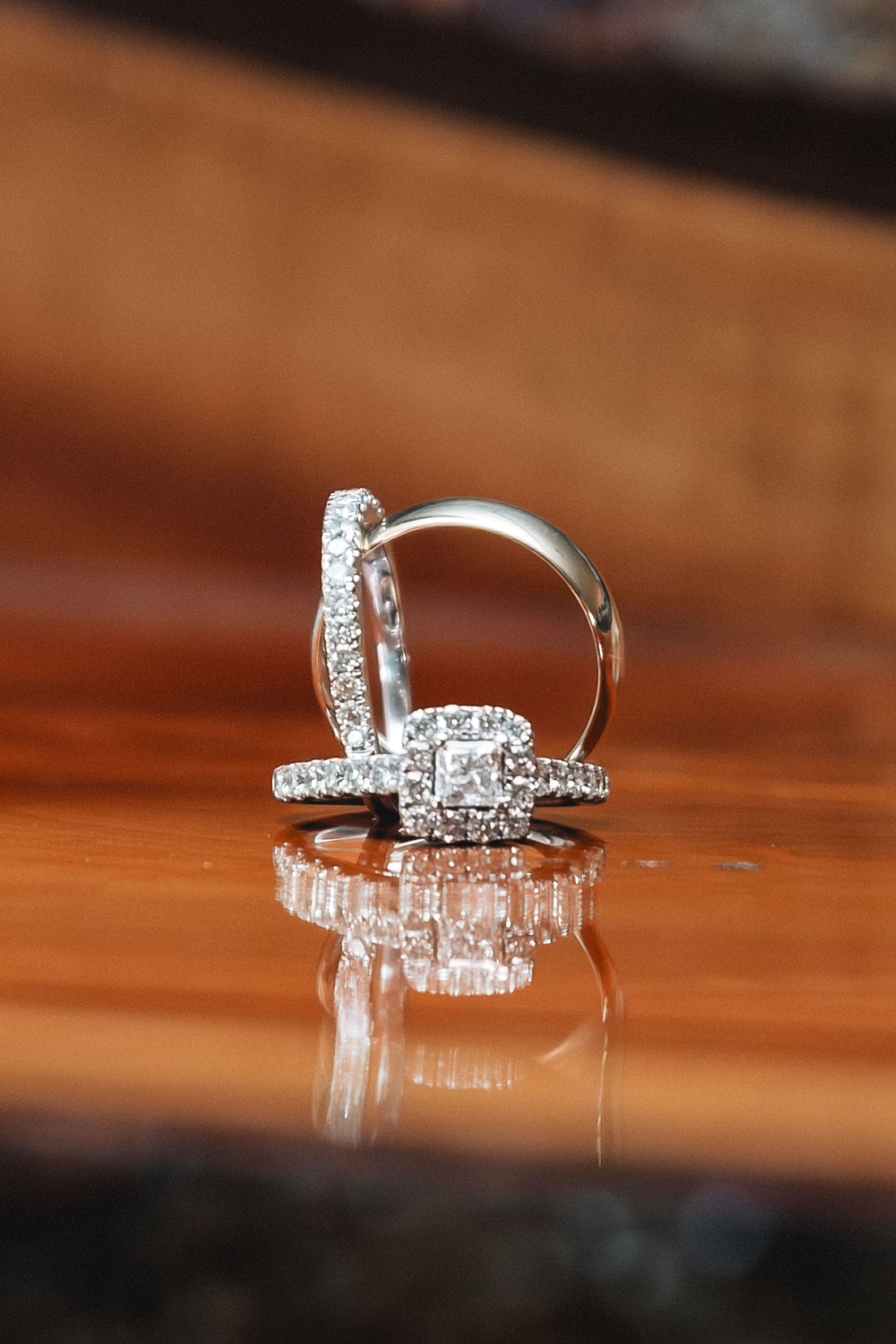 Diamond halo engagement ring and wedding band set displayed upright on reflective wood surface with sparkling brilliance.