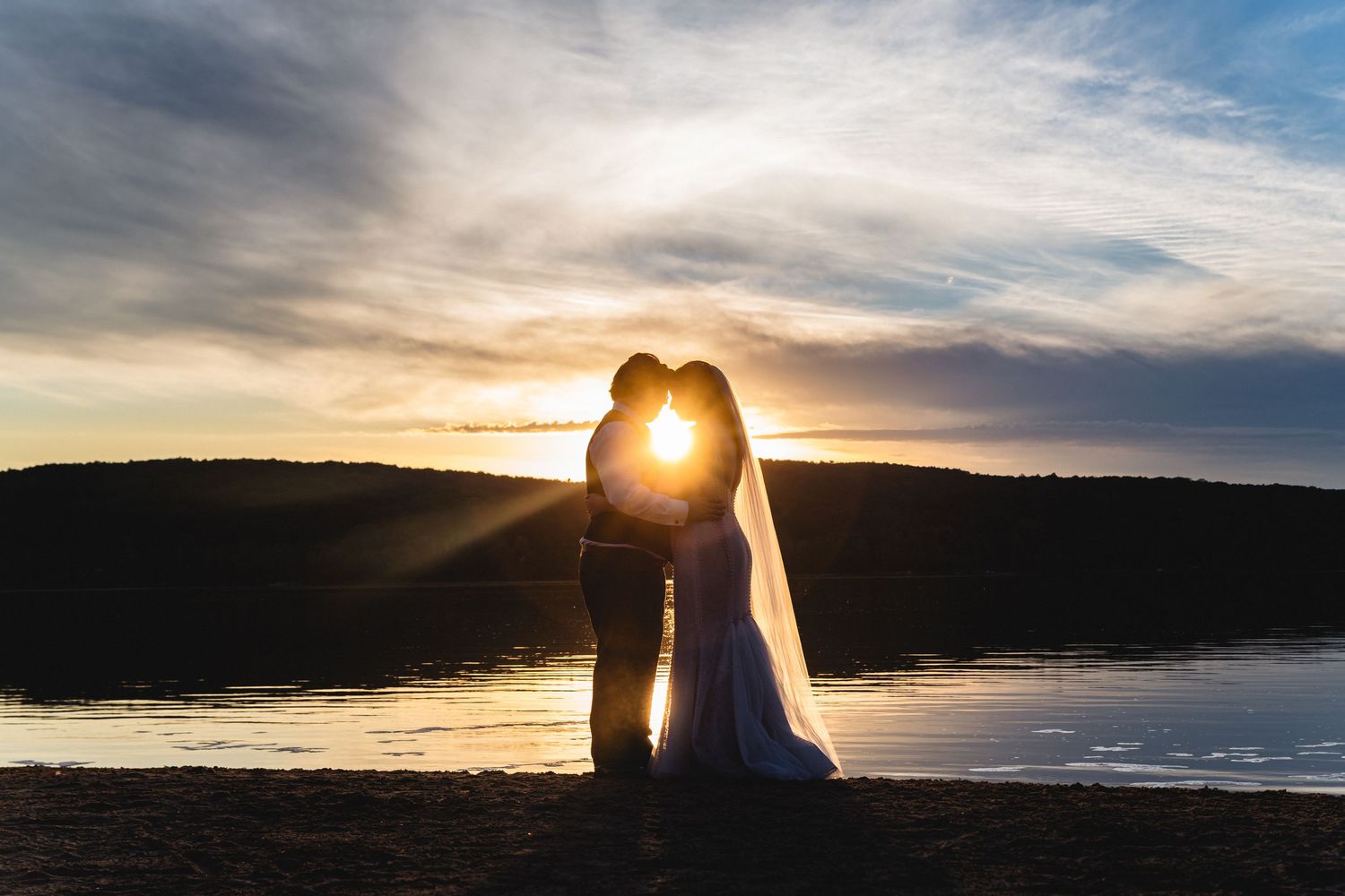 Stunning panoramic sequence of a sunset over a tranquil lake with sunburst through clouds and silhouetted trees.