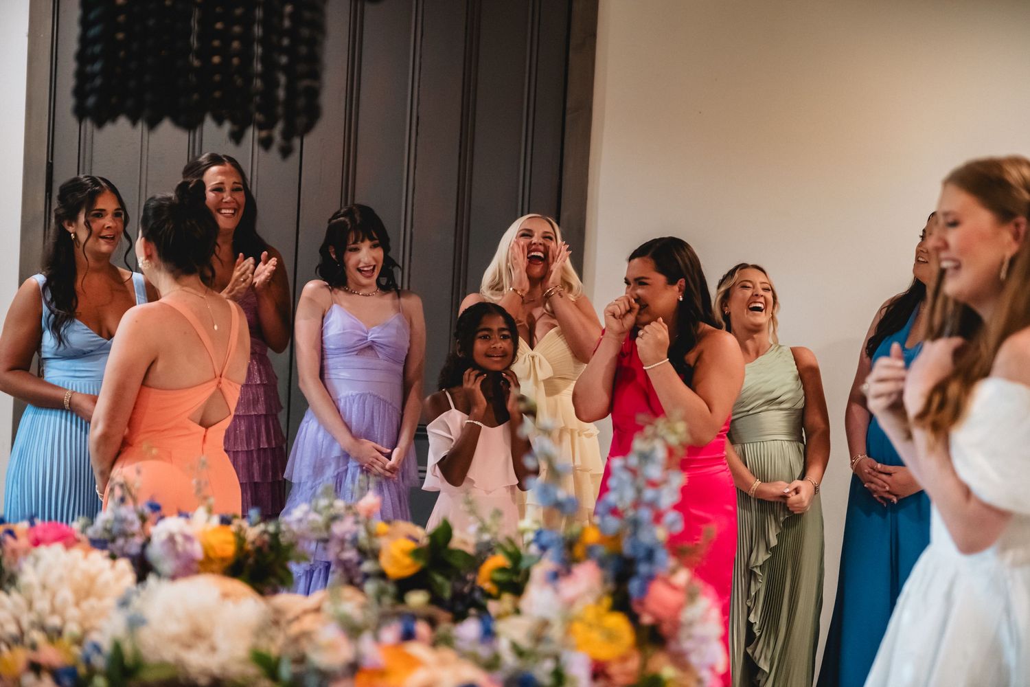Wedding guests in colorful dresses react with joy and excitement during a celebration.