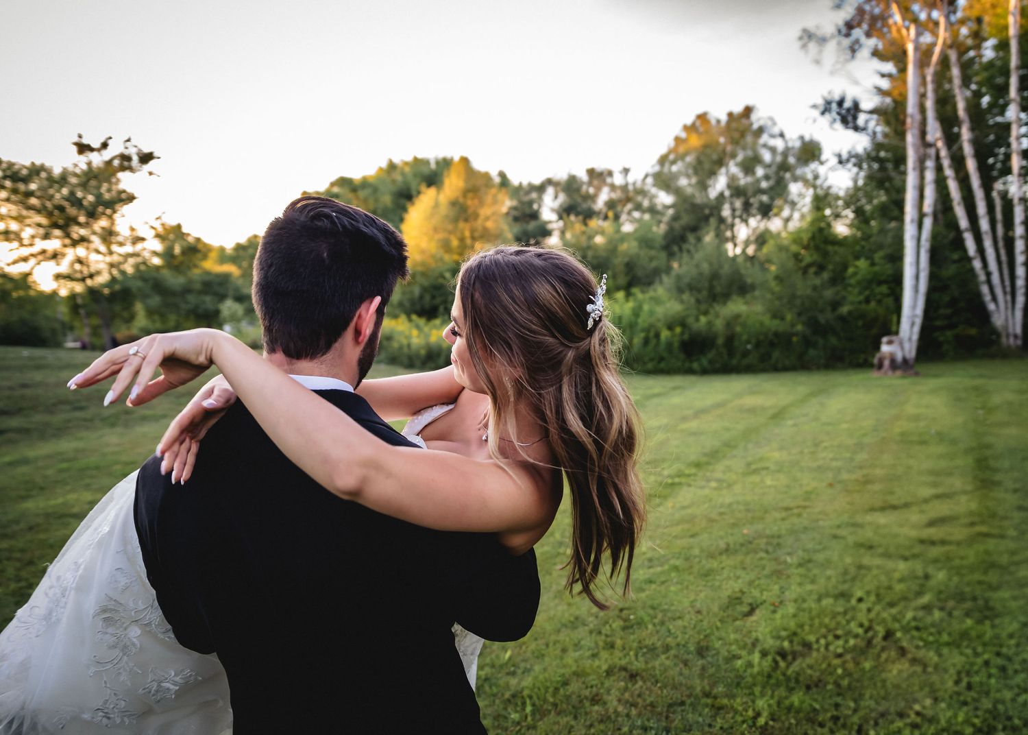 Bride and groom embrace in a sunlit grassy field surrounded by trees during golden hour at Castle Farms