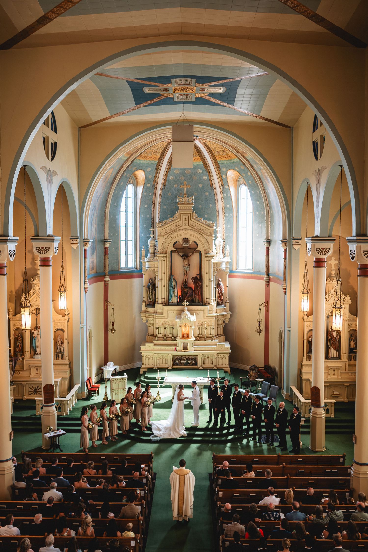 Aerial view of a traditional Catholic church interior during a wedding ceremony with green carpet and ornate altar.