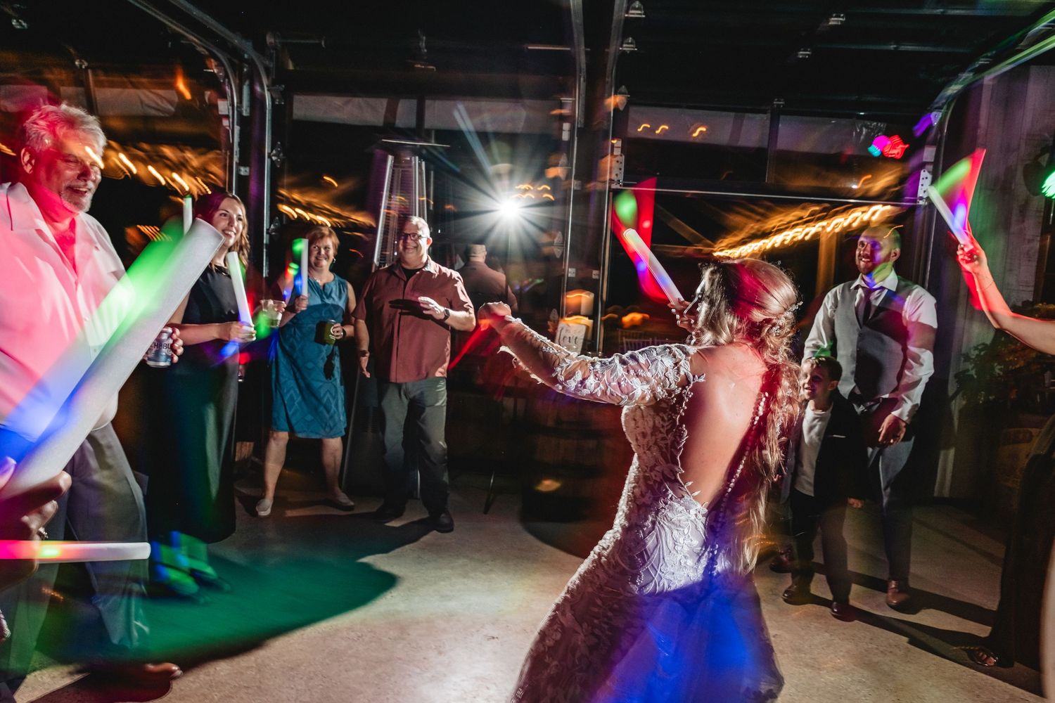 People dance and celebrate on a dimly lit dance floor at a lively wedding reception.
