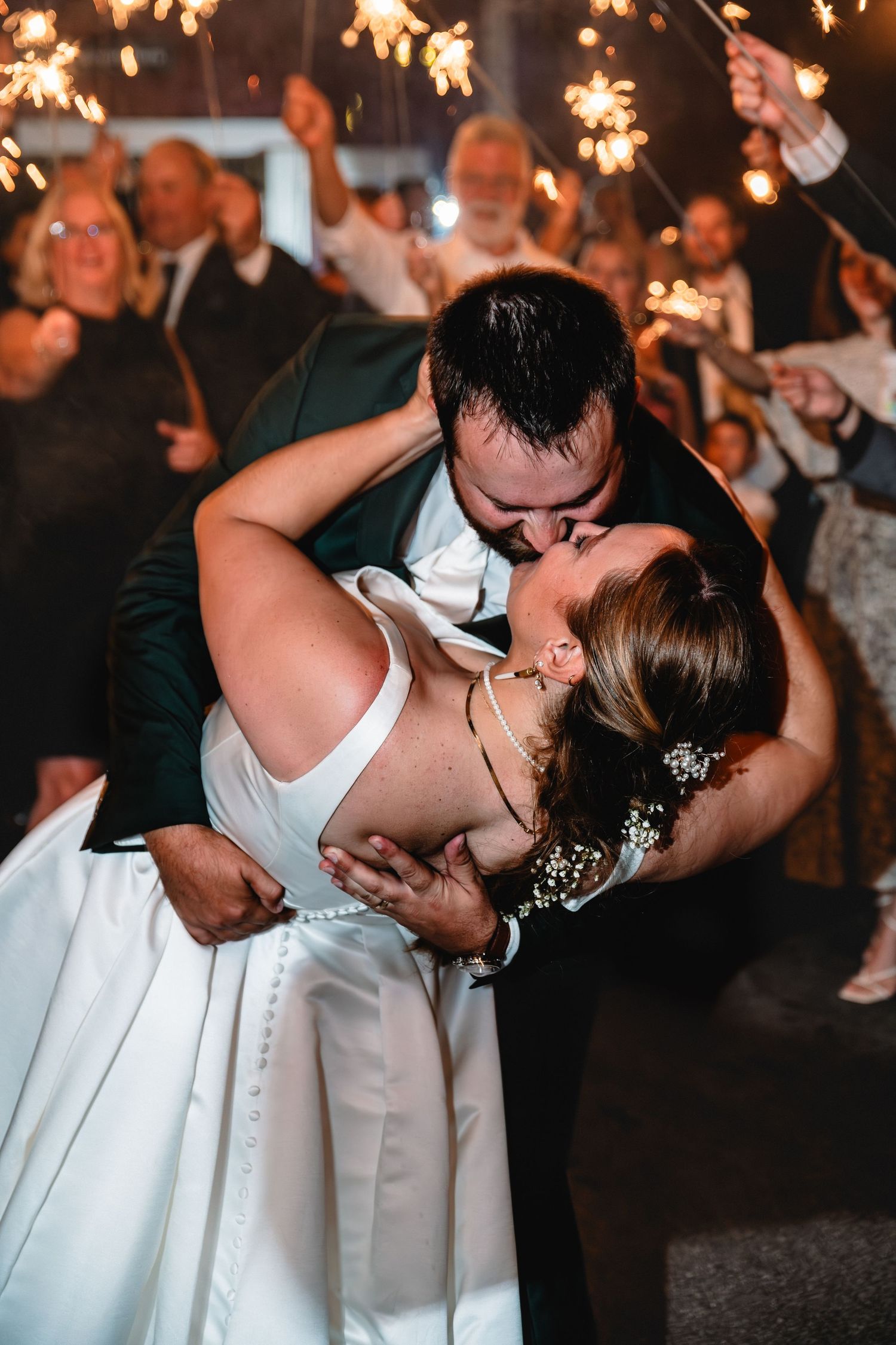 Bride and groom share a romantic dip kiss surrounded by guests holding sparklers at their wedding reception.