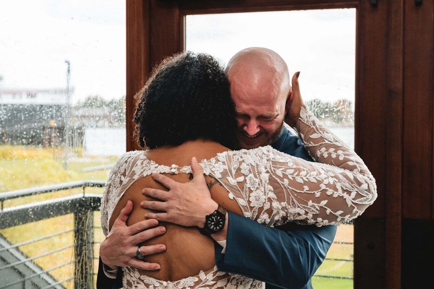 A bride and groom share an emotional hug in a lace wedding dress on a rainy wedding day.